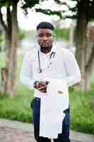 Foto gratuita joven médico afroamericano sostiene bata blanca en la mano con un estetoscopio posado al aire libre