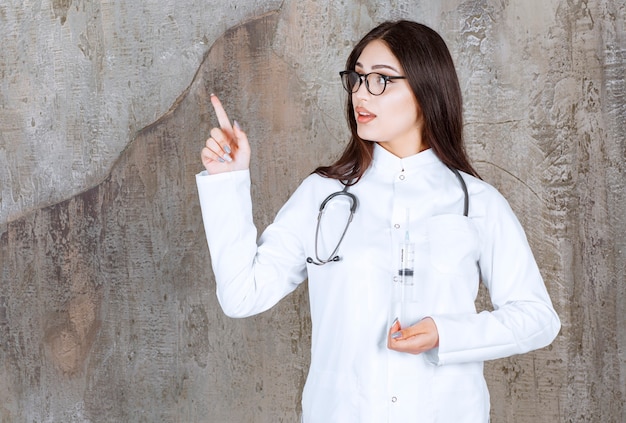 Joven médico apuntando con el dedo hacia arriba en la pared rústica