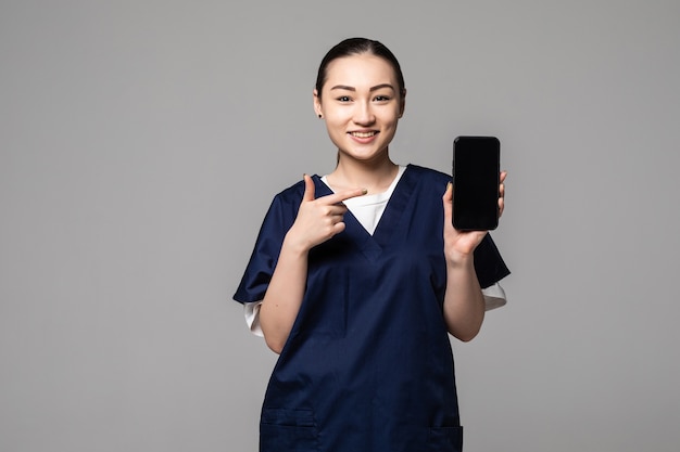 Joven médico asiático señaló en la pantalla con el teléfono inteligente en la pared gris