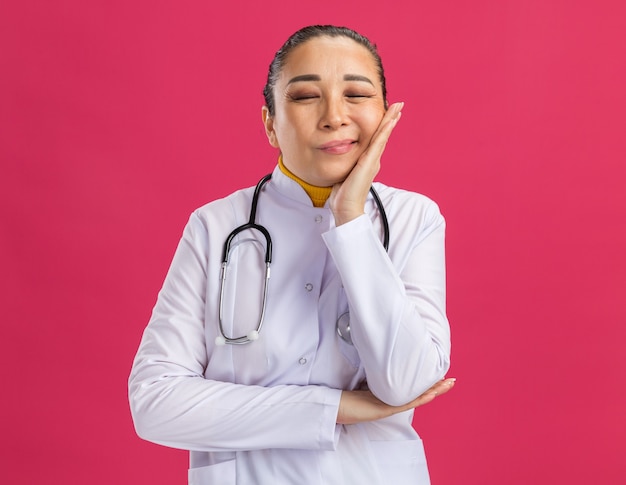 Joven médico con la cabeza apoyada en la palma con los ojos cerrados sintiendo emociones positivas