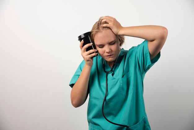 Joven médico con café con dolor de cabeza en blanco.