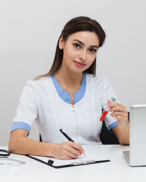 Joven médico escribiendo un informe y sosteniendo una muestra de sangre