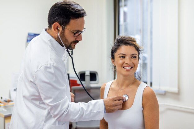 Joven médico escucha el pecho del corazón de una paciente con estetoscopio en la reunión de la clínica