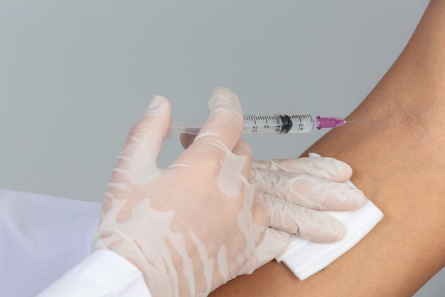 Joven médico está inyectando al paciente con una jeringa hipodérmica en la pared gris.