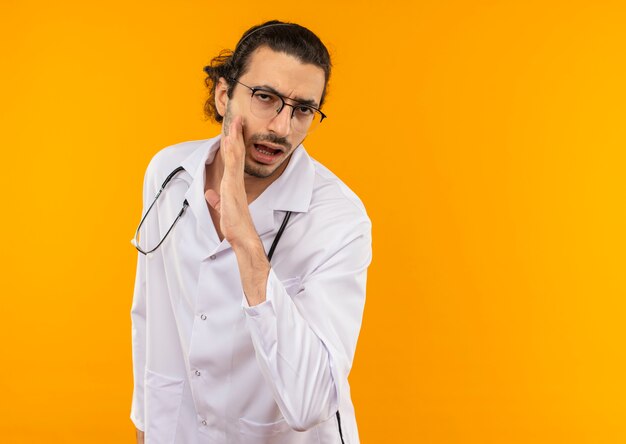 Joven médico con gafas médicas vistiendo bata médica con estetoscopio susurra