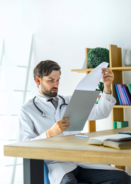 Joven médico leyendo notas en portapapeles