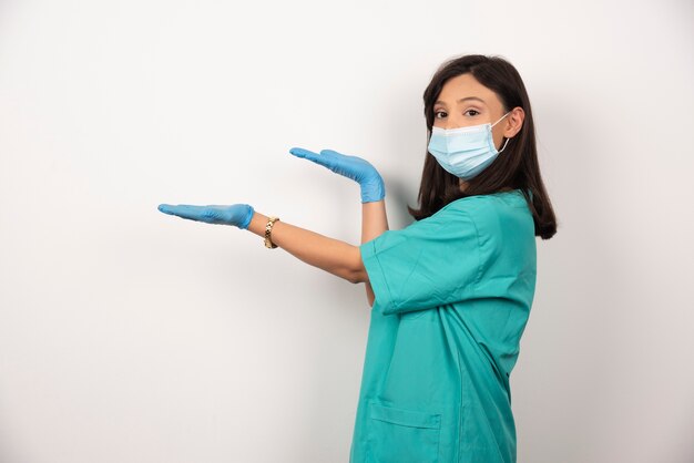 Joven médico en máscara médica y guantes de pie sobre fondo blanco.