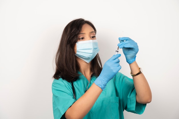 Joven médico en máscara médica y guantes preparando jeringa sobre fondo blanco. Foto de alta calidad