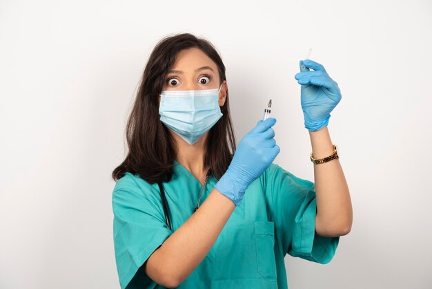 Joven médico en máscara médica y guantes preparando jeringa sobre fondo blanco. Foto de alta calidad