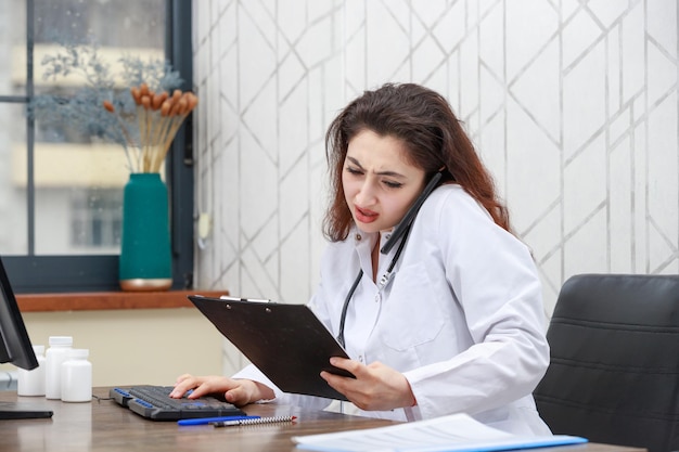 Joven médico mirando la respuesta de la prueba mientras habla por teléfono Foto de alta calidad