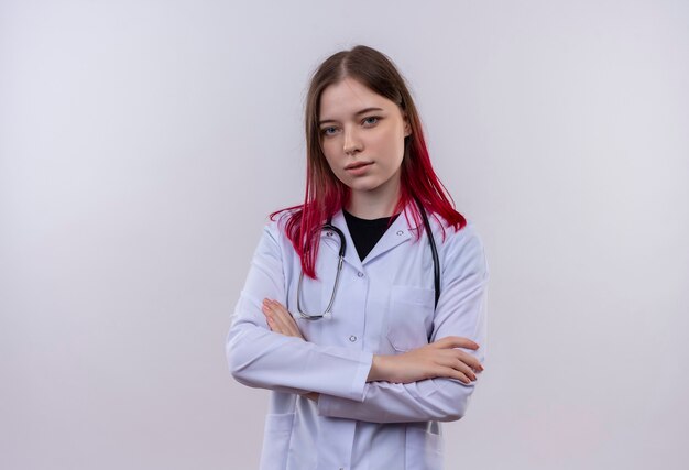 Joven médico mujer vistiendo estetoscopio bata médica cruzando las manos sobre la pared blanca aislada