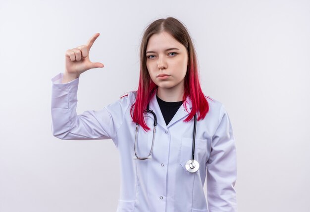 Joven médico mujer vistiendo estetoscopio bata médica fingir sosteniendo algo en la pared blanca aislada