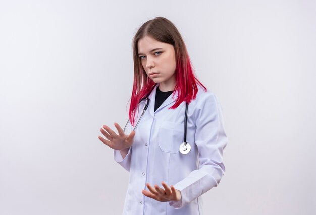 Joven médico mujer vistiendo estetoscopio bata médica mostrando gesto de parada en pared blanca aislada