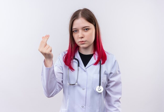 Joven médico mujer vistiendo estetoscopio bata médica mostrando el gesto de la punta en la pared blanca aislada