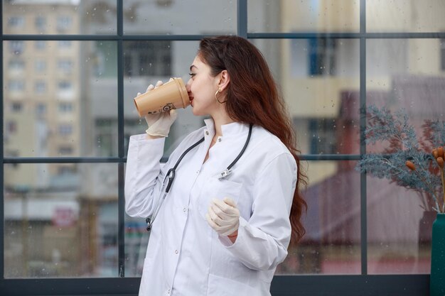 Joven médico de pie y bebiendo café Foto de alta calidad