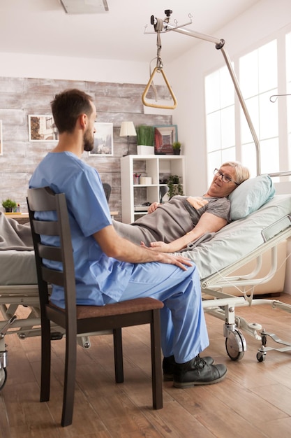 Joven médico sentado junto a una anciana enferma en un hogar de ancianos.