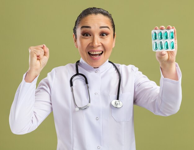 Joven médico sosteniendo blister con pastillas apretando el puño feliz y emocionado