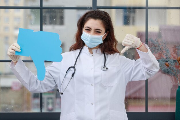 Joven médico sosteniendo una burbuja de idea de papel en forma de pulgar hacia abajo Foto de alta calidad