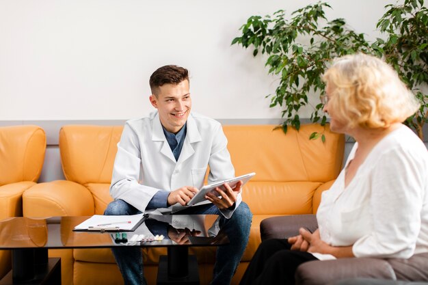 Joven médico sosteniendo una tableta y mirando al paciente