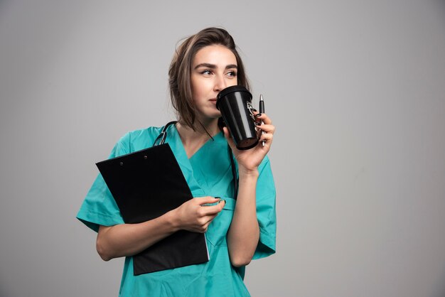 Joven médico tomando café en la pared gris.