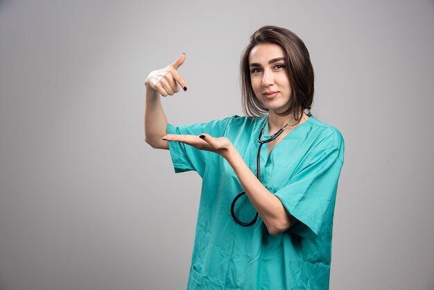 Joven médico en uniforme haciendo gestos en la pared gris.