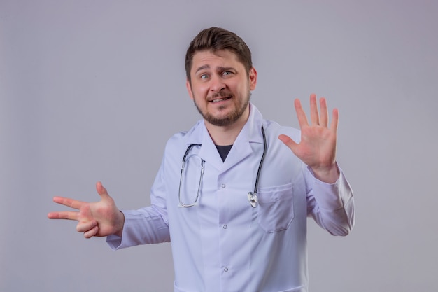 Joven médico vistiendo bata blanca y estetoscopio mirando frustrado mostrando el número ocho con dedos y manos