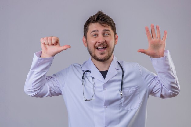 Joven médico vistiendo bata blanca y estetoscopio mostrando el número seis con manos y dedos sonriendo