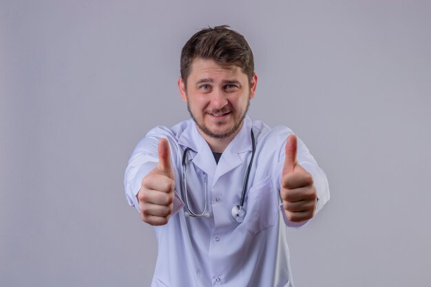 Joven médico vistiendo bata blanca y estetoscopio mostrando pulgares arriba gesto con cara feliz 2