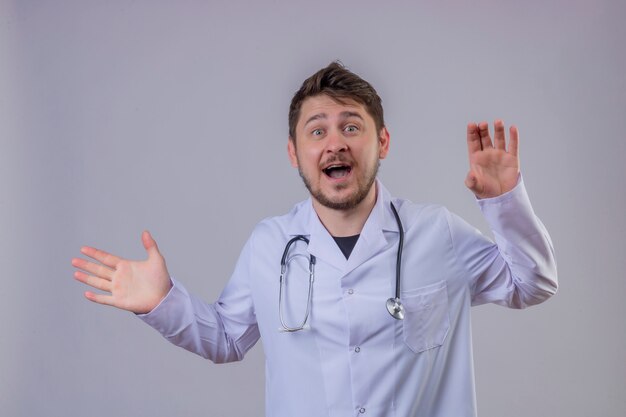 Joven médico vistiendo bata blanca y estetoscopio sorprendido con cara feliz