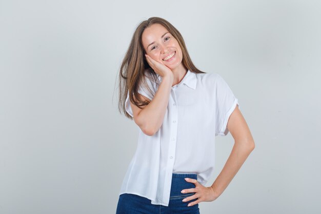 Joven mejilla inclinada sobre la palma levantada en camiseta blanca, jeans y mirando dulce