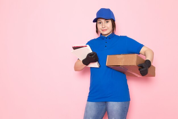 joven mensajero en polo azul gorra azul jeans sosteniendo paquete cuaderno en rosa