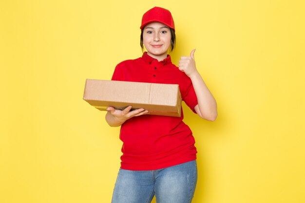 joven mensajero en polo rojo gorra roja blue jeans con paquete sonriendo en amarillo