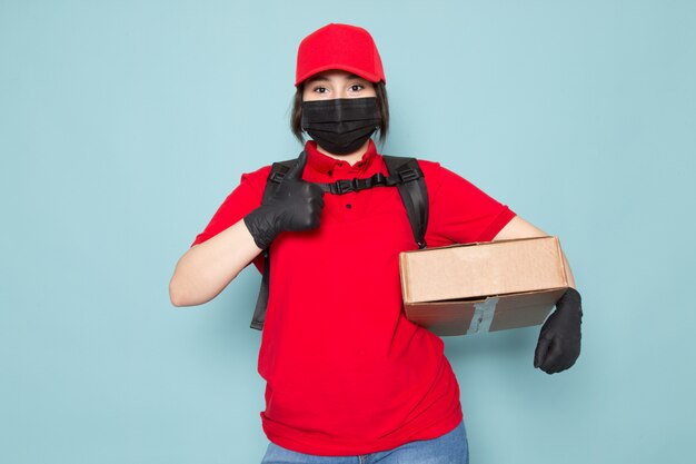 joven mensajero en polo rojo gorra roja máscara protectora estéril negra mochila negra con paquete en azul