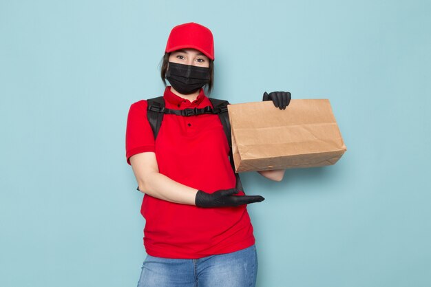 Foto gratuita joven mensajero en polo rojo gorra roja máscara protectora estéril negra mochila negra con paquete en azul