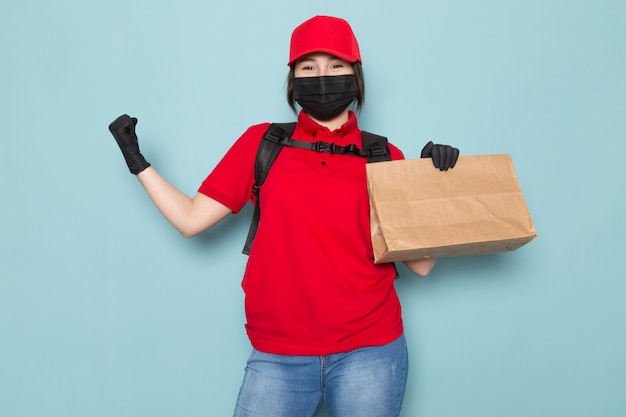 Foto gratuita joven mensajero en polo rojo gorra roja máscara protectora estéril negra mochila negra con paquete en azul