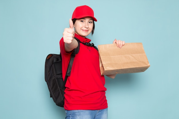 joven mensajero en polo rojo gorra roja mochila negra con paquete sonriendo en azul