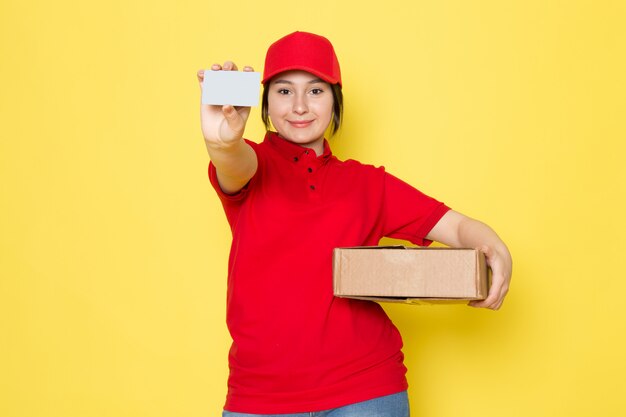 joven mensajero en polo rojo gorra roja con paquete gris tarjeta sonriendo en amarillo