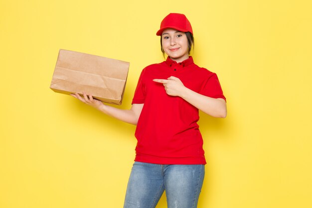 joven mensajero en polo rojo gorra roja con paquete sonriendo en amarillo