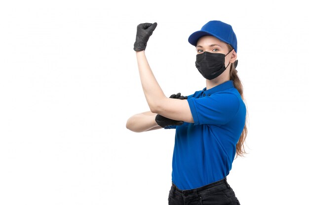 Una joven mensajero de vista frontal en uniforme azul guantes negros y máscara negra posando y flexionando