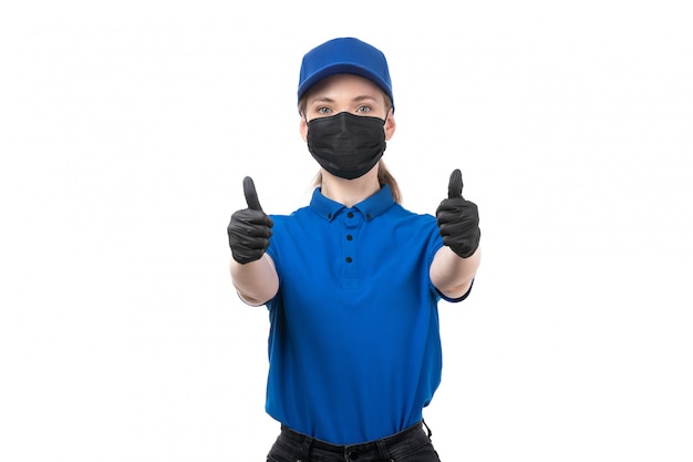 Una joven mensajero de vista frontal en uniforme azul guantes negros y máscara negra posando y mostrando como signo