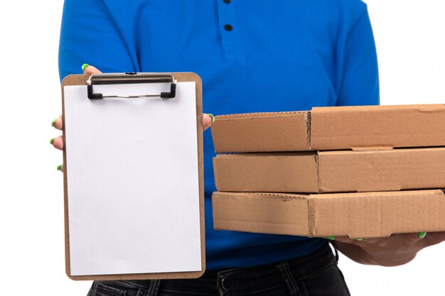 Una joven mensajero de vista frontal en uniforme azul sosteniendo paquetes de entrega de alimentos y bloc de notas para firmas