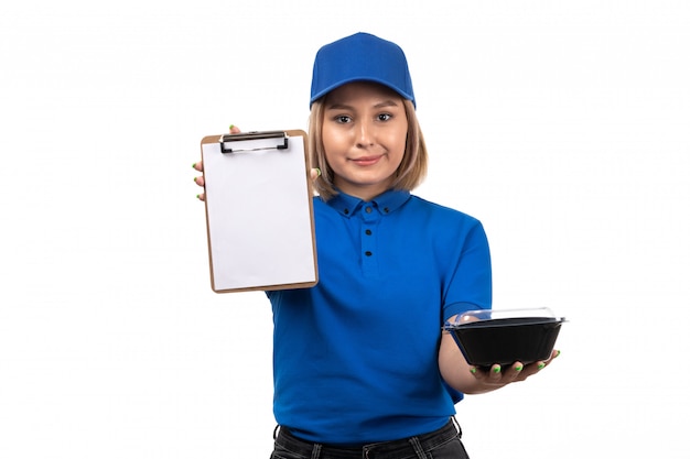 Una joven mensajero de vista frontal en uniforme azul sosteniendo el tazón de entrega de alimentos y el bloc de notas para firmas