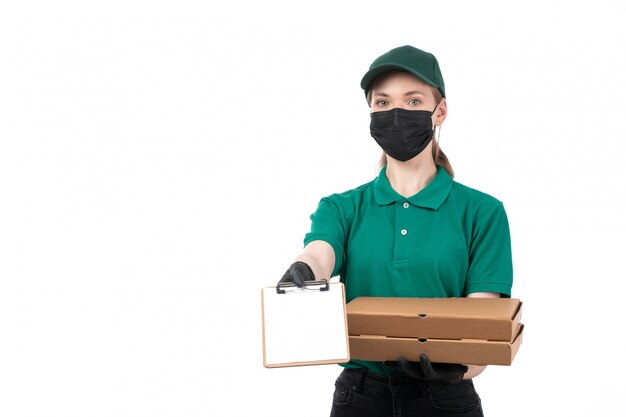 Una joven mensajero de vista frontal en uniforme verde guantes negros y máscara negra con cajas de entrega de alimentos
