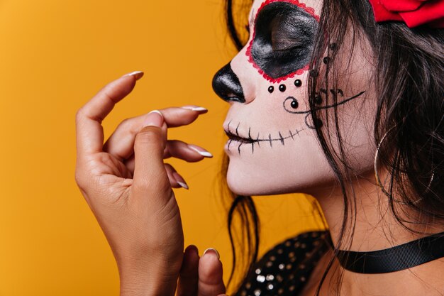 Joven mexicana con rosas en el pelo y arte en forma de calavera en la cara posa linda con los ojos cerrados