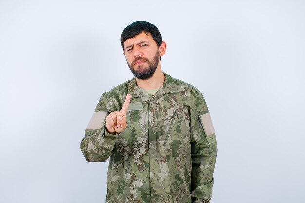 Joven militar está mostrando un gesto de minuto sobre fondo blanco.