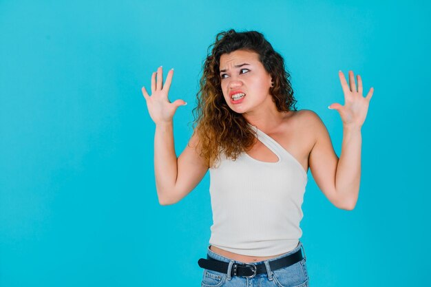 La joven mira a la izquierda levantando las manos sobre fondo azul.