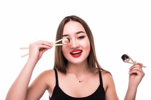 La joven mirada asiática modelo cubre sus ojos con rollos de sushi con palillos de madera