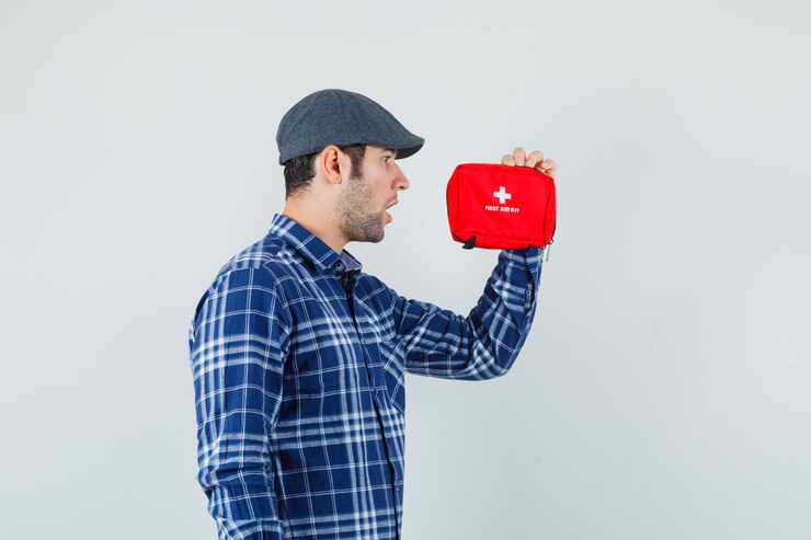 Foto gratuito joven mirando el botiquín de primeros auxilios en camisa, gorra y mirando sorprendido, vista frontal.