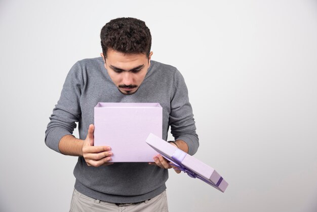 Joven mirando una caja violeta abierta sobre una pared blanca.