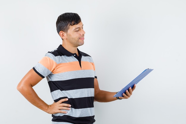 Joven mirando notas en el portapapeles en camiseta y mirando positivo